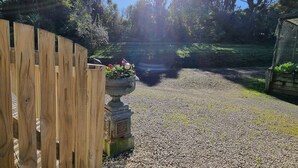 A gravel pathway leading to a wooden fence and a garden area with a decorative urn and flowers.