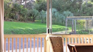 A wooden deck with a chair and a table, overlooking a well-maintained garden with various plants and a glass structure.