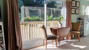 A room with a large sliding glass door leading to a balcony, a wooden table with chairs, a bookshelf, and a clock on the wall.