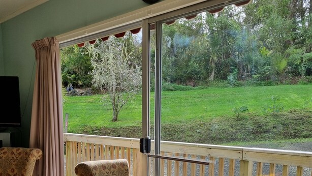 A room with a wooden table, two chairs, a TV, and a large window overlooking a garden.