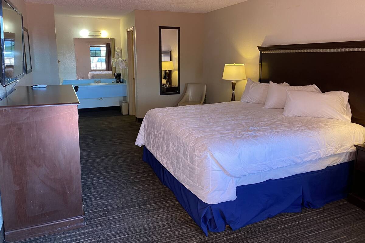Une chambre d’hôtel avec un grand lit, un bureau, une chaise, un miroir et une salle de bain visible au fond.