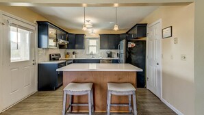 A modern kitchen with dark cabinets, a large island, and pendant lighting. - Splash and Go | 1135 ft from the beach | Private Pool, Hot Tub | Nags Head (Nags Head)