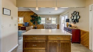 A spacious kitchen with a large island, wooden cabinets, pendant lighting, and a view into the dining area. - Splash and Go | 1135 ft from the beach | Private Pool, Hot Tub | Nags Head (Nags Head)