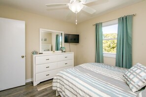 Een slaapkamer met een bed, een dressoir, een televisie en een raam met gordijnen.