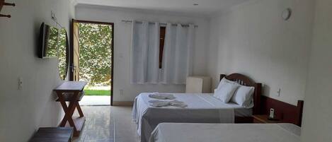 A hotel room with two beds, a small table, a bench, a TV, and a window with curtains.