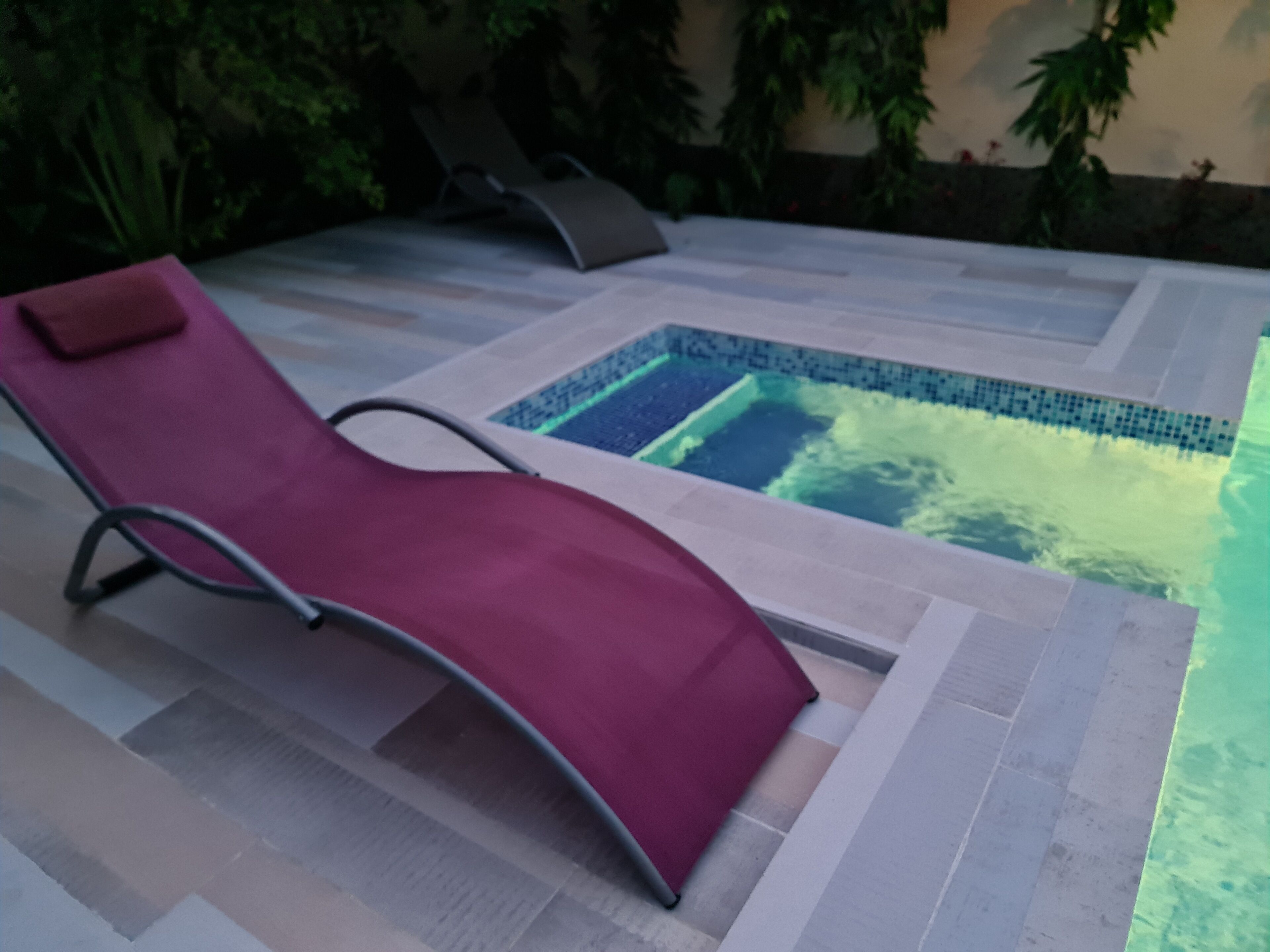 Una silla de relax roja junto a una piscina pequeña con borde de azulejos.