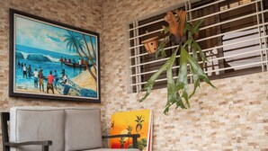A room with a brick wall, a framed painting of a beach scene, a sofa, and a window with blinds. - Villa Jaddis (Abidjan)