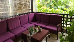 A purple sofa set with a table and plants, a wooden ceiling, and a view of greenery outside. - Villa Jaddis (Abidjan)
