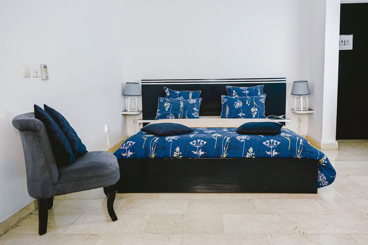 Un dormitorio con una cama, dos mesitas de noche, una silla y una lámpara.