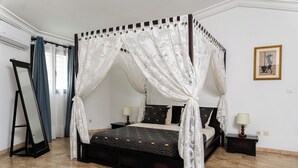 A four-poster bed with a canopy, a bedside table with a lamp, and a framed picture on the wall. - Villa Jaddis (Abidjan)