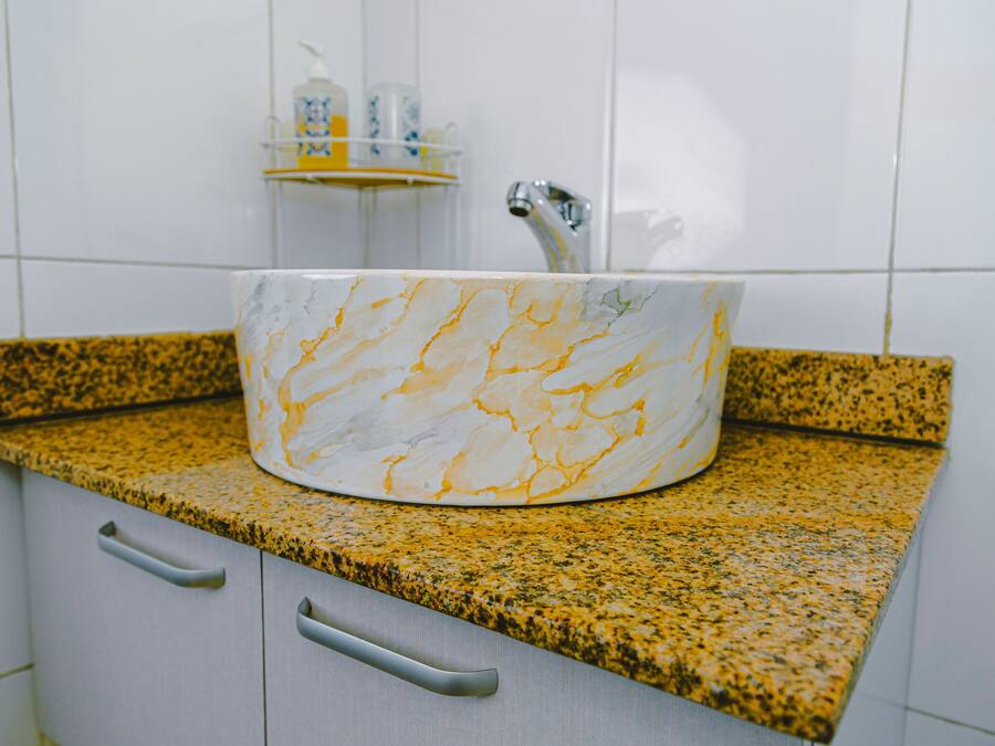 A bathroom with a marble sink, granite countertop, and a white tiled wall.