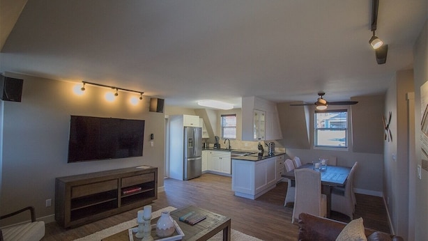 A modern living room with a flat-screen TV, wooden entertainment unit, and a dining area with a table and chairs.