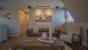 A living room with a brown leather sofa, a white armchair, a wooden coffee table, and a painting of boats on the wall.