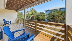 Una terraza techada al aire libre con barandillas de madera, sillas Adirondack azules y vistas a un barrio residencial con árboles y una casa azul.