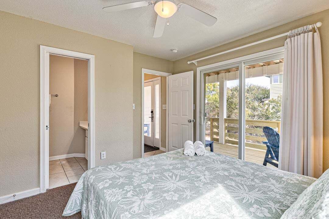 Un dormitorio con cama, ventilador de techo y vistas al exterior a través de un ventanal corredera.