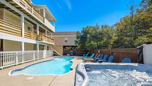 Un área de piscina y jacuzzi con sillas reclinables y una terraza de madera.
