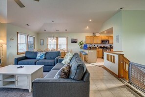 A modern living room with a gray sofa, a white coffee table, and a kitchen area with wooden cabinets and a microwave. - Debo's Tiki Hut (Corolla)