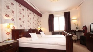 Een hotelkamer met een groot bed, twee nachtkastjes, een bureau, een stoel, een televisie en een raam met gordijnen.