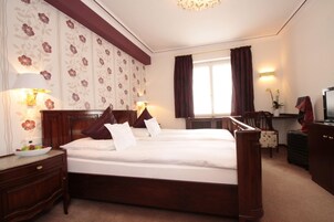 Habitación de hotel con una cama grande, dos mesitas de noche, un escritorio, una silla, un televisor y una ventana con cortinas.