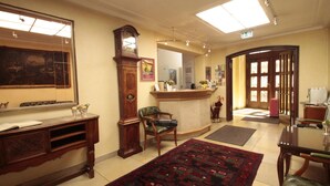Een hotellobby met een receptiebalie, een grote klok, een schilderij, een kamerbreed tapijt met dessin en een eetgedeelte.