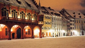 Een sneeuwbedekt plein met historische gebouwen, waaronder een opvallend rood pand met gebogen ramen en een balkon.