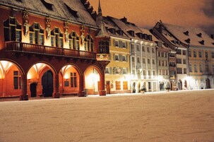 Un edificio histórico con ventanas arqueadas y un balcón, rodeado de calles nevadas en la noche.