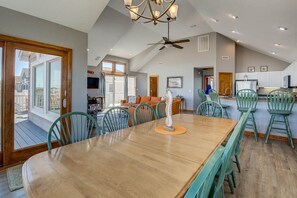 A spacious dining area with a wooden table and chairs, a ceiling fan, and a view of the outside through large windows. - Krosnest | Oceanfront | Private Pool, Hot Tub | Nags Head (Nags Head)