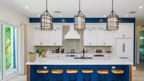 Une cuisine moderne avec des meubles blancs, un grand îlot central doté de tabourets et un éclairage suspendu.