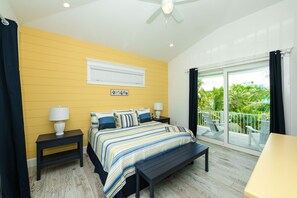 A bedroom with a bed, bedside tables, a bench, a ceiling fan, and a balcony with a view of greenery. - Palmetto Pointe! 5BR Luxury Home with Pool, Spa, Rooftop Deck and Walk to Beach (Anna Maria)