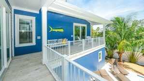 Une maison à deux étages, avec une façade bleue, un balcon doté de balustrades blanches et un petit espace piscine.