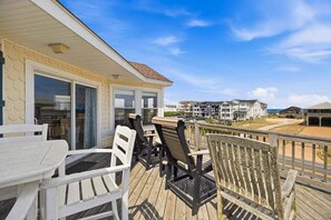 A wooden deck with outdoor furniture, a glass door entrance, and a view of beachfront buildings.