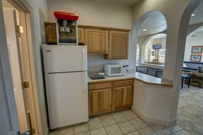 Kitchen area with a refrigerator, microwave, and wooden cabinets, offering a doorway to a dining area with an outside view.