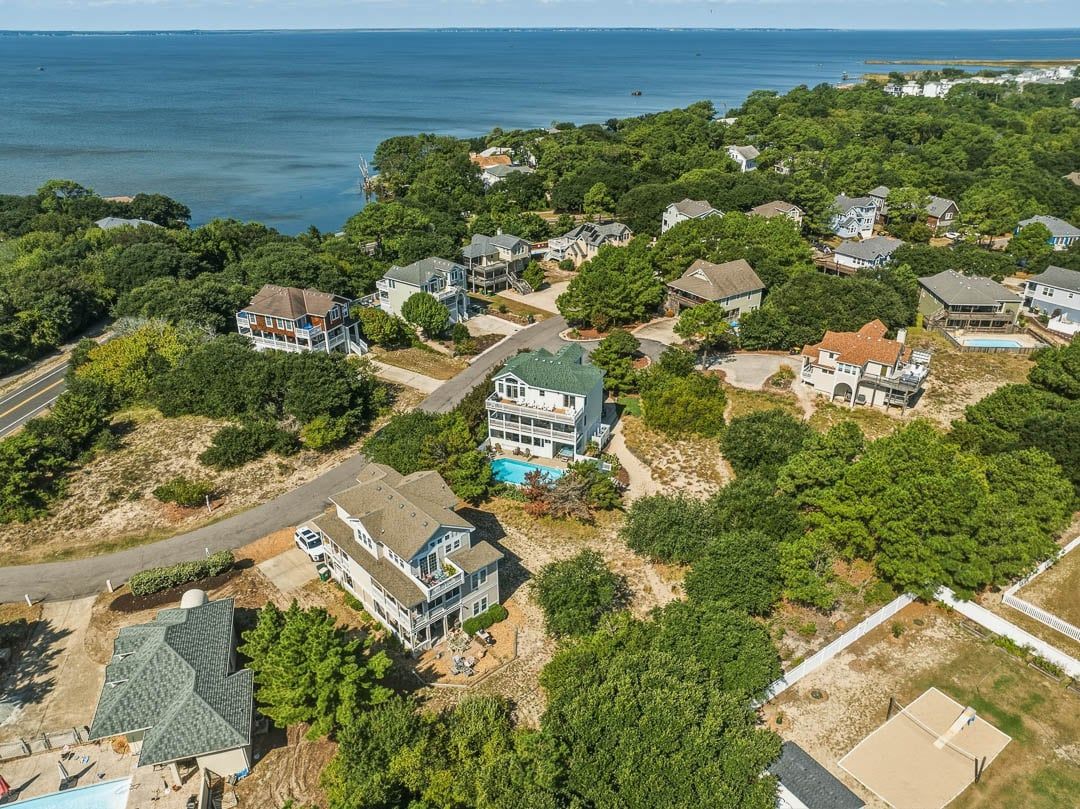 An aerial view of a residential area with houses, a swimming pool, and a large body of water in the background.