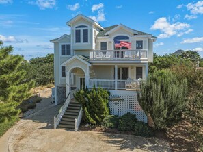 A two-story house with a balcony, a flag, and a staircase leading to the entrance. - A Pirate's Paradise | 1499 ft from the beach | Dog Friendly, Private Pool, Hot Tub | Corolla (Corolla)