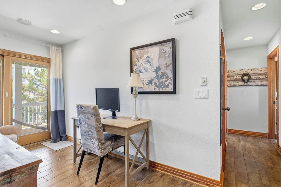 A room with a desk, chair, computer, lamp, and a painting on the wall.