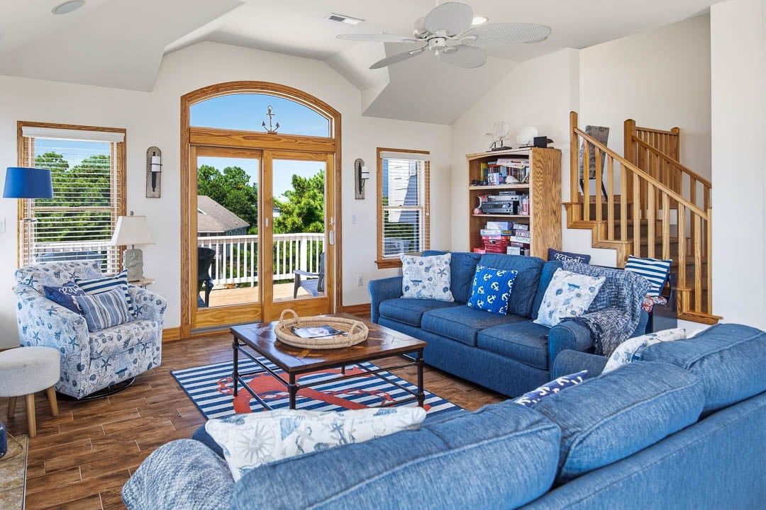 Un salon spacieux avec un canapé bleu, une table basse en bois et une vue sur une terrasse extérieure, accessible par une porte vitrée.