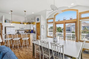 A modern kitchen with white cabinets, a dining area with a white table and chairs, and large windows with a view of the neighborhood. - A Pirate's Paradise | 1499 ft from the beach | Dog Friendly, Private Pool, Hot Tub | Corolla (Corolla)