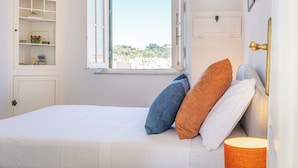 A bedroom with a bed, pillows, a lamp, a wardrobe, and a window with a view. - Rental In Rome Sistina View Terrace Apartment (Rome)