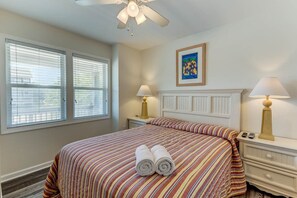 Une chambre à coucher avec un grand lit, deux tables de chevet avec des lampes, un ventilateur de plafond et un tableau au mur.
