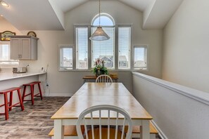 Une cuisine avec une table à manger, des tabourets rouges et une fenêtre avec des stores.