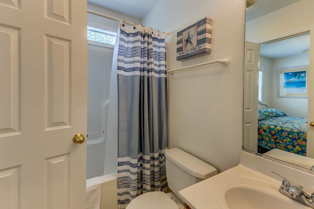 A bathroom with a striped shower curtain, a toilet, a sink, and a mirror.