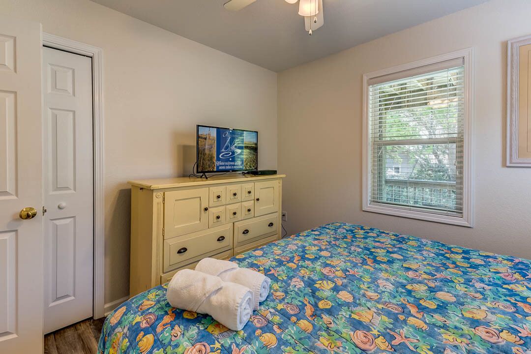 Un dormitorio con una cama, un aparador, un televisor y una ventana con persianas.