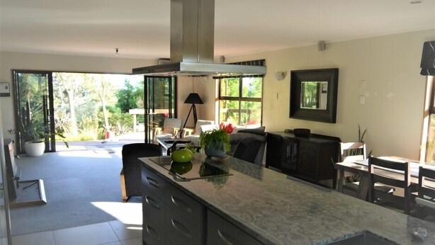A modern kitchen with a large island, a dining area with a table and chairs, and a view of the outdoors. - Our Tree house, private rural retreat . (Whakatane)