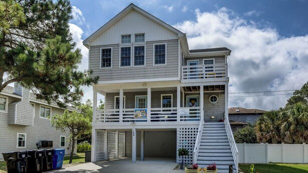 A two-story house with a front porch, a covered garage, and a staircase leading to the second floor. - Loafing Around In Duck | 1250 ft from the beach | Private Pool, Hot Tub | Duck (Duck)