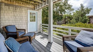 A covered porch with wicker furniture and a door. - Loafing Around In Duck | 1250 ft from the beach | Private Pool, Hot Tub | Duck (Duck)