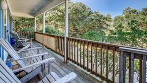 Un terrazza in legno con ringhiera, affacciata su un giardino con diverse piante e alberi.