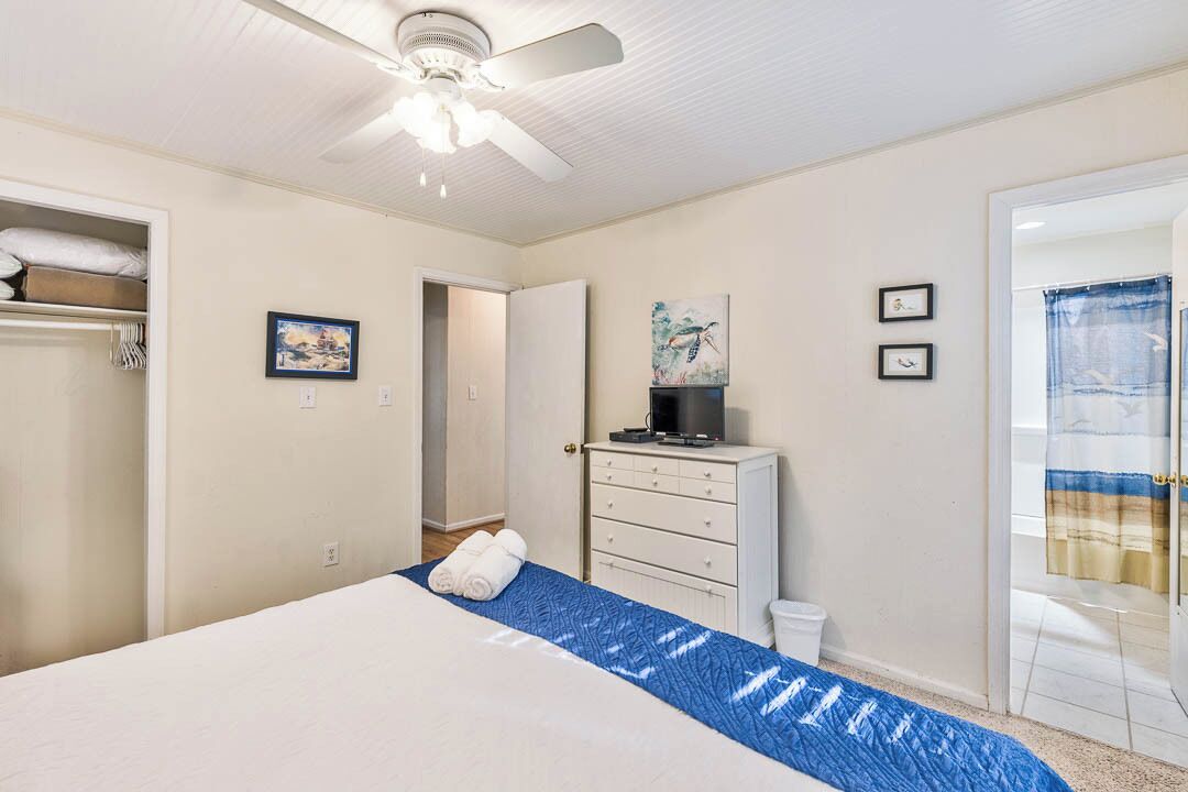 A bedroom with a bed, a ceiling fan, a dresser, and a television.
