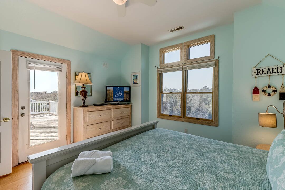 A bedroom with a bed, a dresser, a television, and a window with a view.