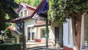 Una casa de dos pisos con un porche cubierto, una escalera y un árbol en primer plano.