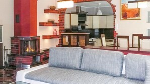 Una sala de estar con chimenea, un sofá y una zona de cocina visible a través de un arco.